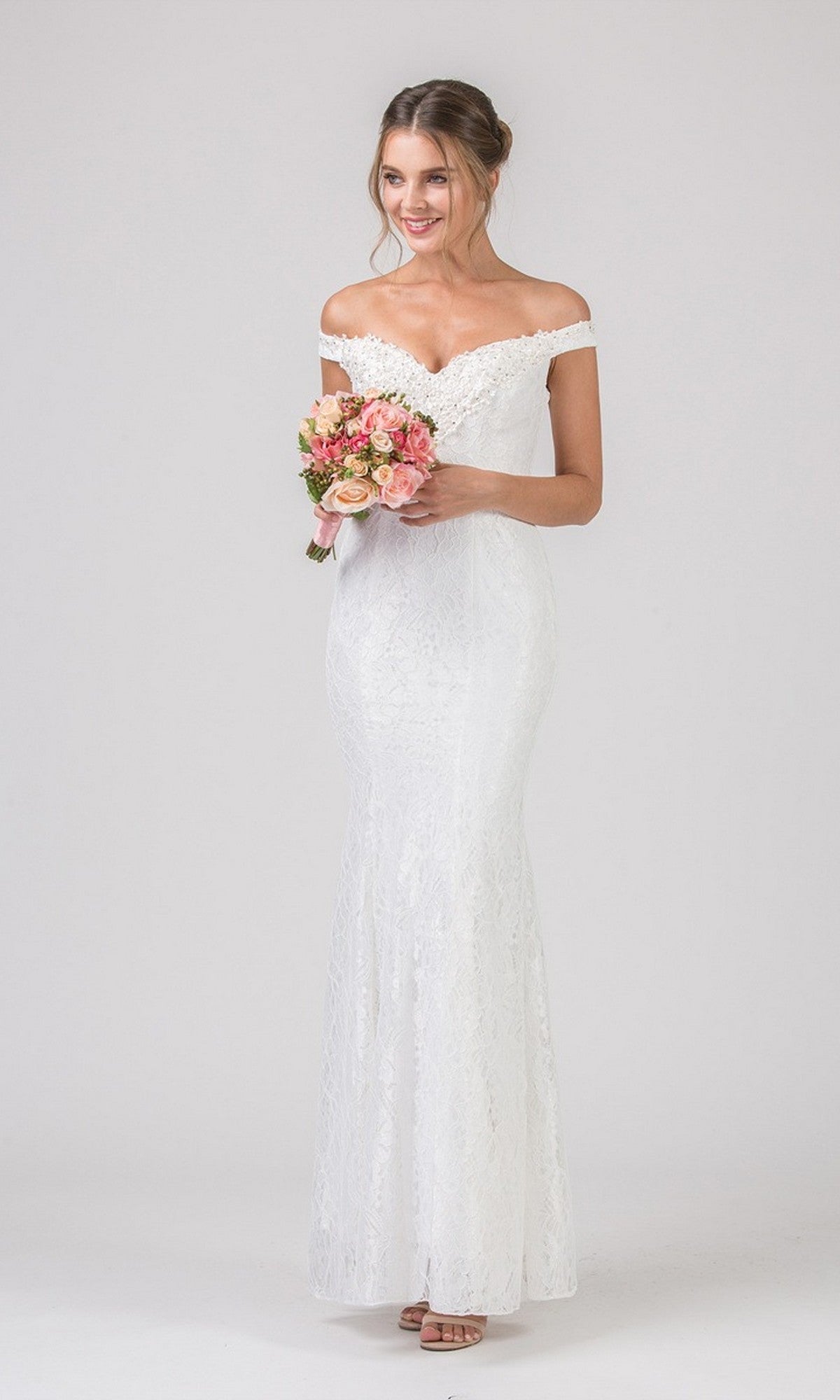A woman in the off white Long Prom Dress: Eureka 8030 holds a small bouquet of pink and peach flowers, standing against a plain light background.